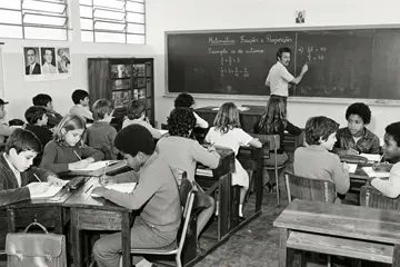 Foto de arquivo em preto e branco: turma em sala de aula, com a professora escrevendo uma lição de matemática no quadro